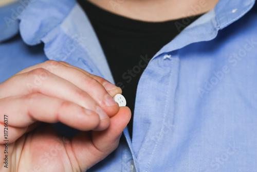 Ripped shirt. Man holds loose button. Clothes needs repairing and sewing.