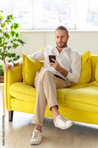 Photo of businessman holding cellphone while sitting on sofa in apartment