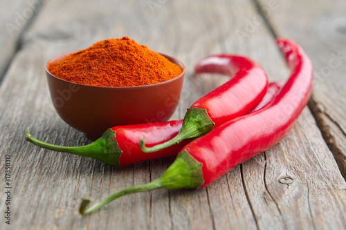 Whole and ground to powder red chili pepper on wooden kitchen table.