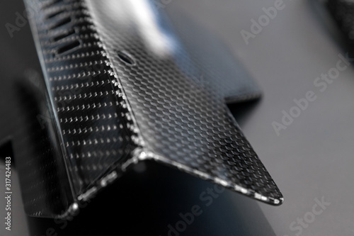 A close-up on a car exterior elements made from carbon fiber of interwoven black and gray color from heavy-duty yarns for the production of light and durable elements in industry. Tuning body parts.