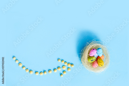 plane flies on blue background.yellow sweets. Direction sign for easter eggs. Spring and Easter are coming.Beautiful creative arrow made of colored eggs. Pointer or cursor from eggs. Top view flat.