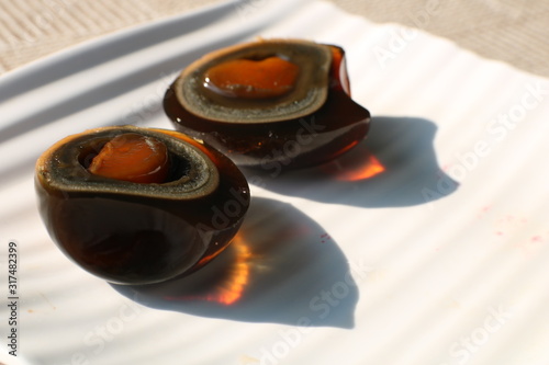 Two halves of black fermented century egg lying on white plate with bright beautiful shadows. Traditional chineese food