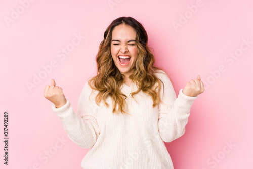 Young curvy woman posing in a pink background isolated cheering carefree and excited. Victory concept.