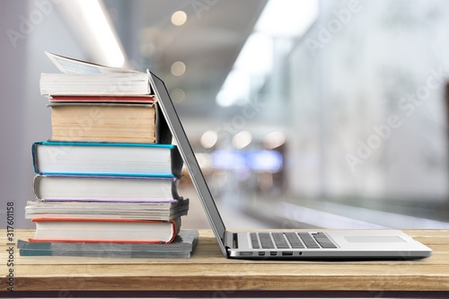 Stack of books with laptop on wooden table