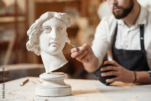 Skillful sculptor makes professional restauration of gypsum sculpture of woman's head at the creative workshop.