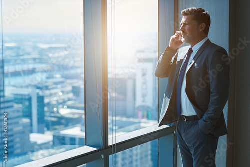 Mature business CEO talking on phone alongside large high windows