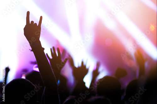 Audience with hands raised at a music festival and lights streaming down from above the stage. Crowd raising their hands, dancing and enjoying great the concert.