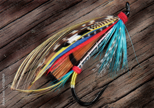A closeup pic of a colourful fly fishing lure on a rough wooden surface
