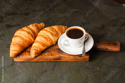 Espresso in a white cup and two croissants on a dark background, on wooden board, place for text, view from the top