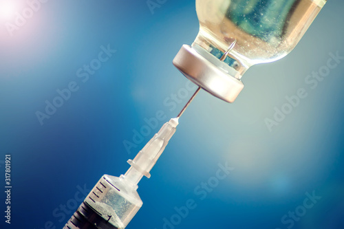 A bottle with vaccine and syringe in front of blue background. Medicine, science and healthcare concept