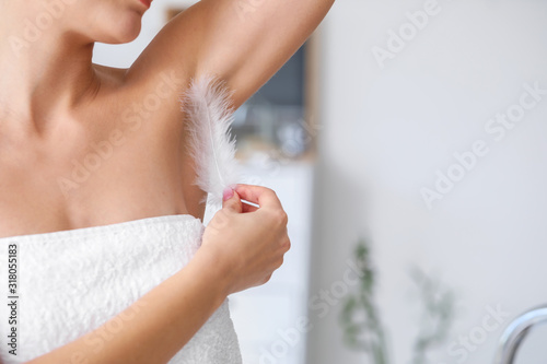 Beautiful young woman with feather in bathroom, closeup. Concept of using deodorant