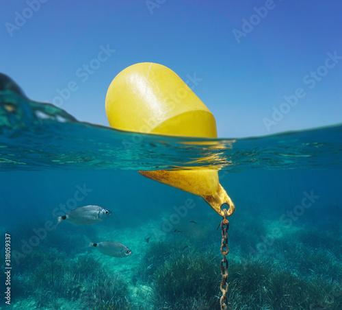 A yellow beacon buoy in the sea for beach marking and cross channel limits with blue sky and fish underwater, split view half over and under water surface, Mediterranean, Spain