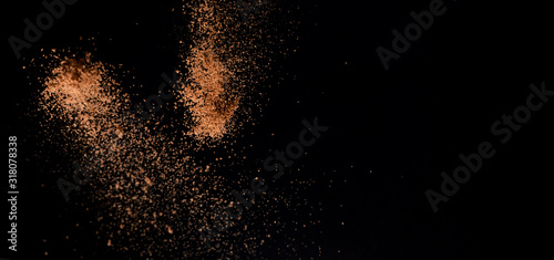 Cocoa powder explosion in motion on black background. Chocolate dust. Wide banner.