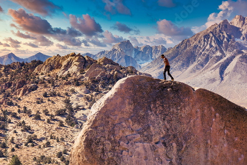 Man rock climbs on huge granite boulder in the Buttermilk area of Bishop, California with the Sierra Nevada behind