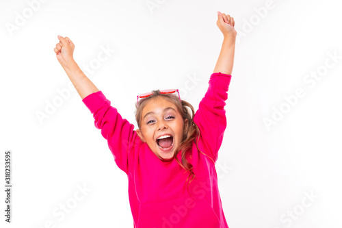 charming Caucasian girl in a pink sweater sincerely rejoices and smiles happily raising her hands up on a white background with copy space