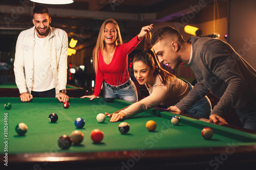 Group of friends play billiards at night out