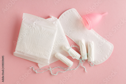 menstruation cycle, feminine hygiene and protection products, sanitary pads, tampons and menstrual cup on pastel pink background, top view, flat layout