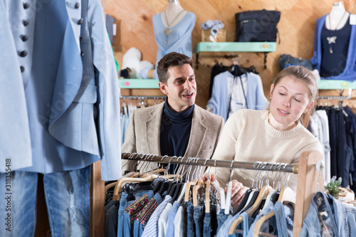 Smiling woman and man are choosing variety clothes on hanger