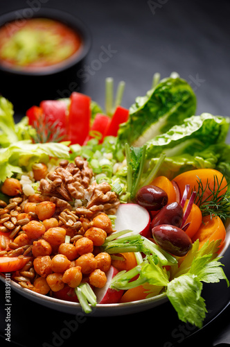 Healthy salad with various vegetables, seeds and herbs on a black background, close up. The concept of healthy eating