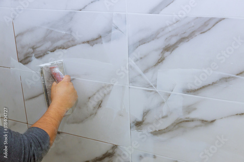 Male hand with the rubber applies grout on a seam between tiles