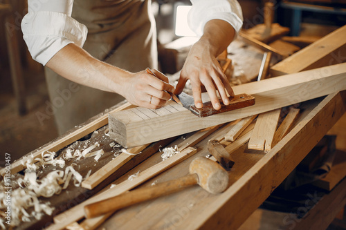 Man working with a wood. Carpenter in a white shirt