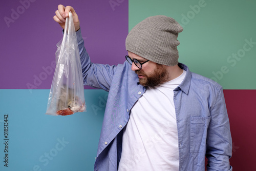 Man with dislike looking at the stinking fish in a transparent bag.