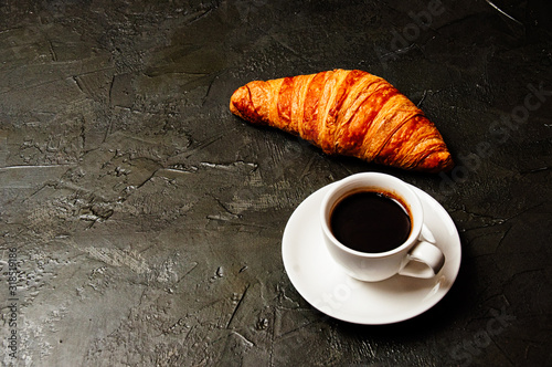 Croissant and espresso on dark gray concrete background with a place to insert text from the left. The concept of a delicious breakfast, business lunch or coffee break.