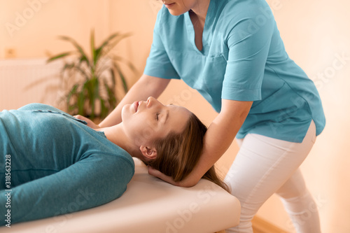 Female physiotherapist or a chiropractor adjusting patients neck. Physiotherapy, rehabilitation concept. Side view cropped shot.