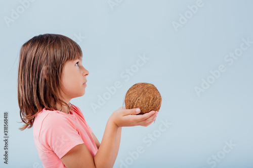 girl with coconut in hand. isolated on blue background, copy space, in studio, profile view