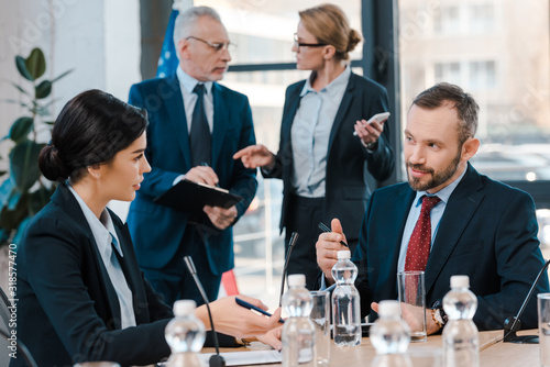 selective focus of diplomats talking and gesturing near glasses on table