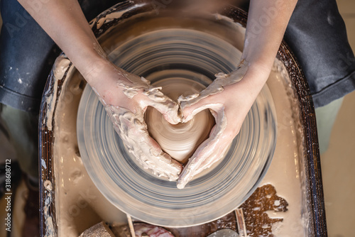 Potter working with clay on a Potter's wheel. Women's hands show a heart sign. Concept of love for pottery art