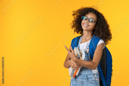Cute smiling little african american schoolgirl with books on yellow background