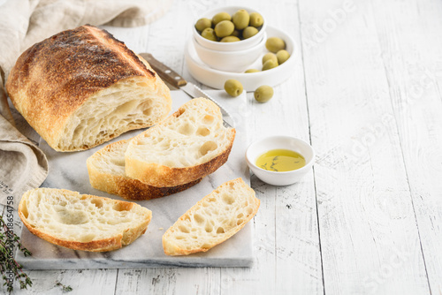 Ciabatta. Italian bread with olive oil, herbs and olives on a marble table. Space for text