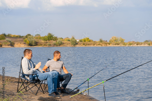 leisure and people concept. Happy friends with fishing rods on pier by lakeside.