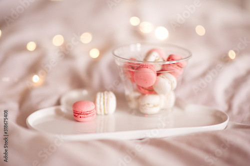 Tasty macaroon cookies on white plate in glass bottle over glowing lights closeup. Good morning.