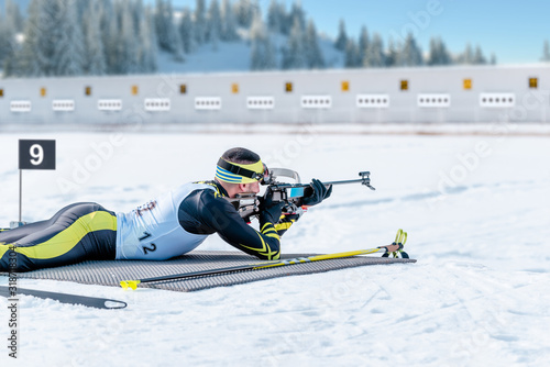 Biathlete lies and shoots a target at a 20 km race. Athlete with modern sports equipment for competition