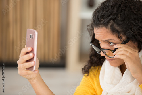 annoyed upset woman in glasses looking at smartphone with frustration