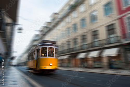 Yellow electric tram drive fast on old streets and colorful buildings of Lisbon, Portugal, digital motion blur.