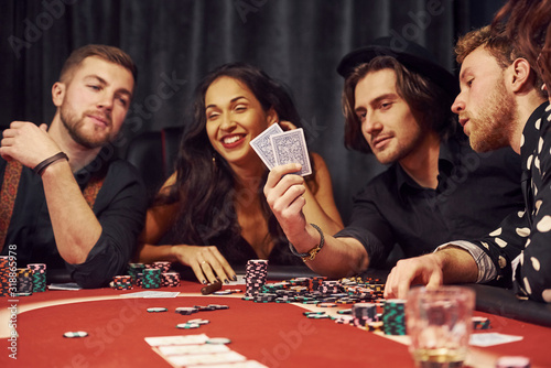 With glasses of drink. Group of elegant young people that playing poker in casino together