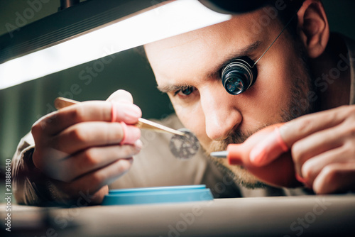 Selective focus of watchmaker working with watchpart and blower by lamp on table