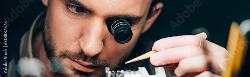 Panoramic shot of watchmaker in eyeglass loupe working with wristwatch isolated on black