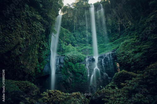 Hiker standing in front of huge Jungle waterfall surrounded by lush jungle vegetation and flora in Bali, Indonesia. Travel survival, lifestyle concept. Beautiful Sekumpul waterfall on Bali