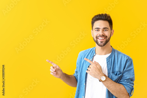 Handsome young man pointing at something on color background