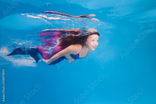 girl in a mermaid costume poses underwater in a pool.