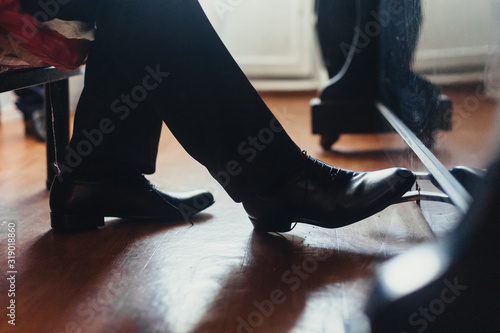 A male musician plays the piano, presses the foot in black shoes on the pedal close-up. Photography, concept.