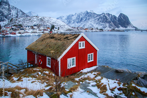 Red rorbu along the coast of Reine in the Lofoten Islands archipelago, Northern Norway in winter - View over the fjord from a traditionnal fishing hut during the polar night in the Arctic