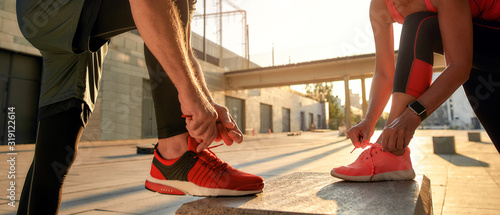 Active morning. Close up photo of two people in sport clothes tying shoelaces before running together outdoors