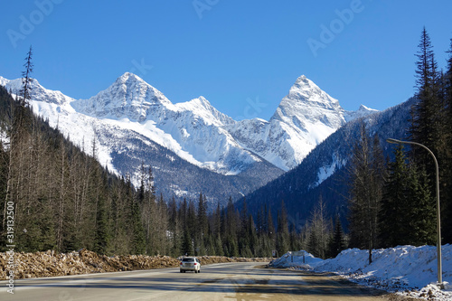 Dirty white SUV drives along a scenic highway running under the snowy mountains