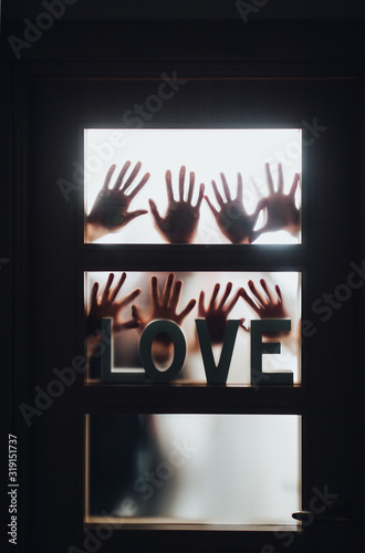 Word - LOVE. Hands and fingers of people in silhouette against the background of a door with a window, locked and asking for help. Horror. Swingers, group sex, swedish family, relax and orgy concept.