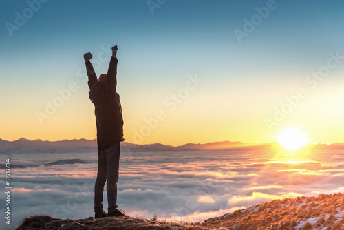 A man stands high in the mountains, at sunset, above the clouds.